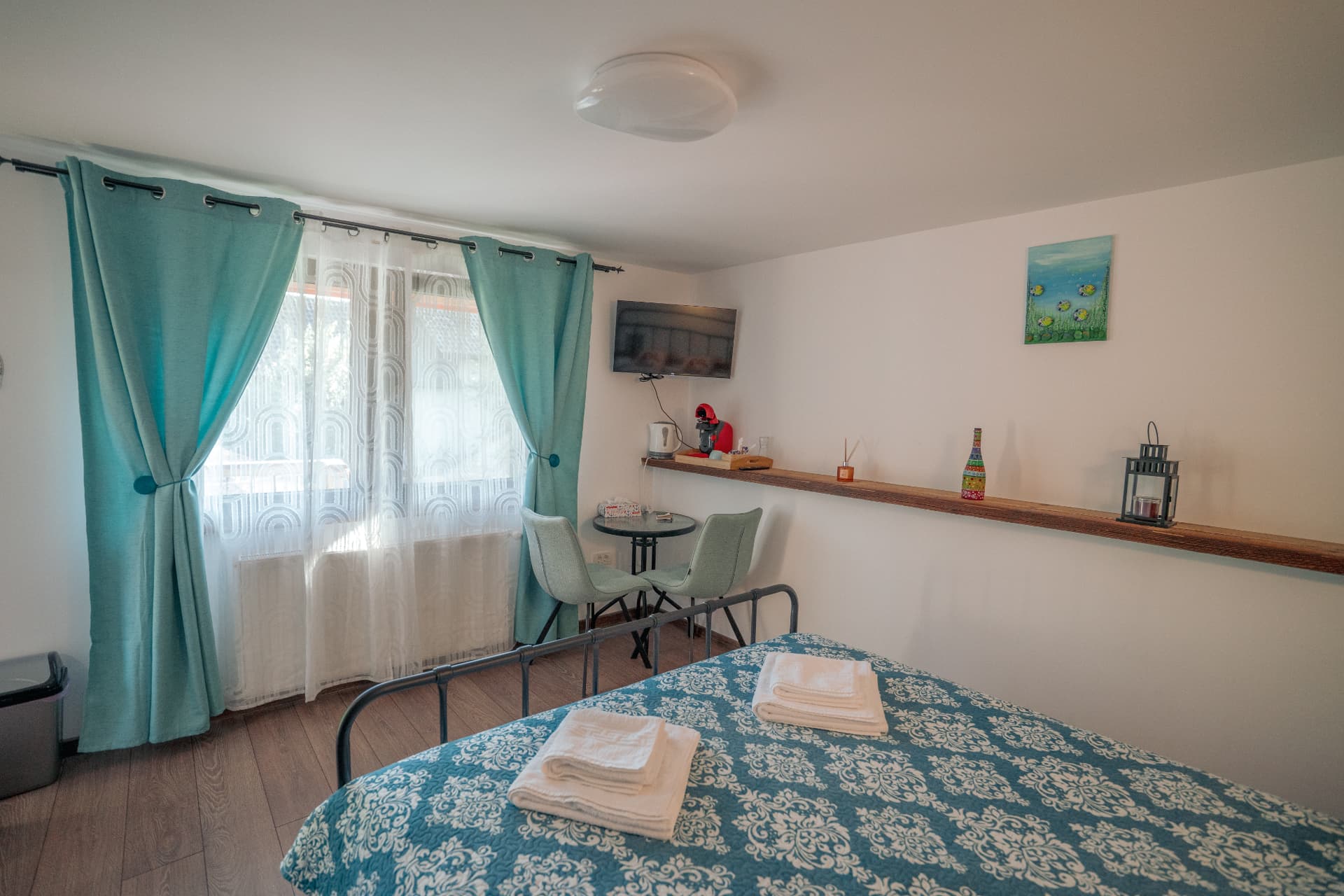 Camera cu draperii turcoaz, colț de cafea și pat pregătit
